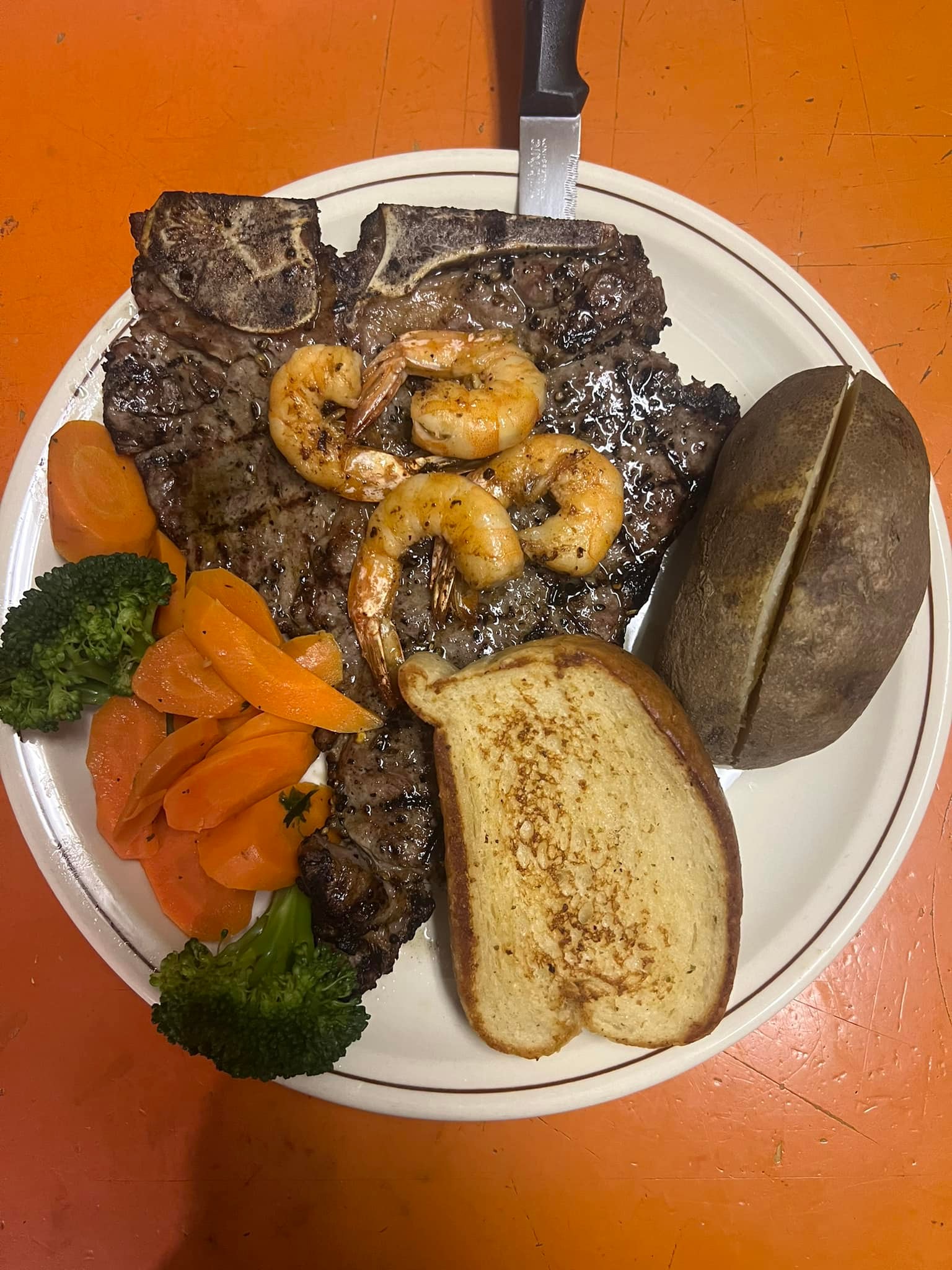 overview of a dinner plate with steak, baked potato, shrimp, and fresh vegetables, cooked by the Luso Ladies in Kitimat